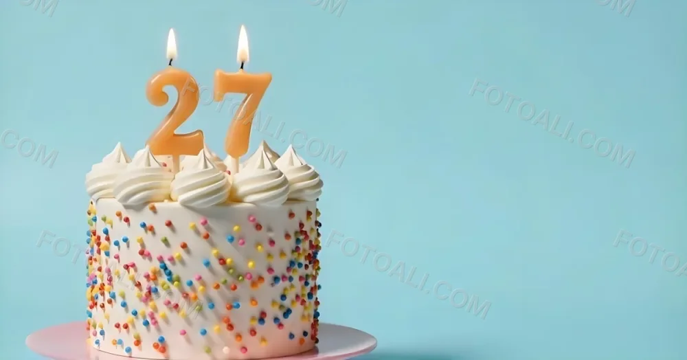A Cake With White Frosting And Colorful Sprinkles Topped With Two Lit Candles Shaped Like The Numbers 2 And 7 On A White Plate With A Pink Background 5 18db