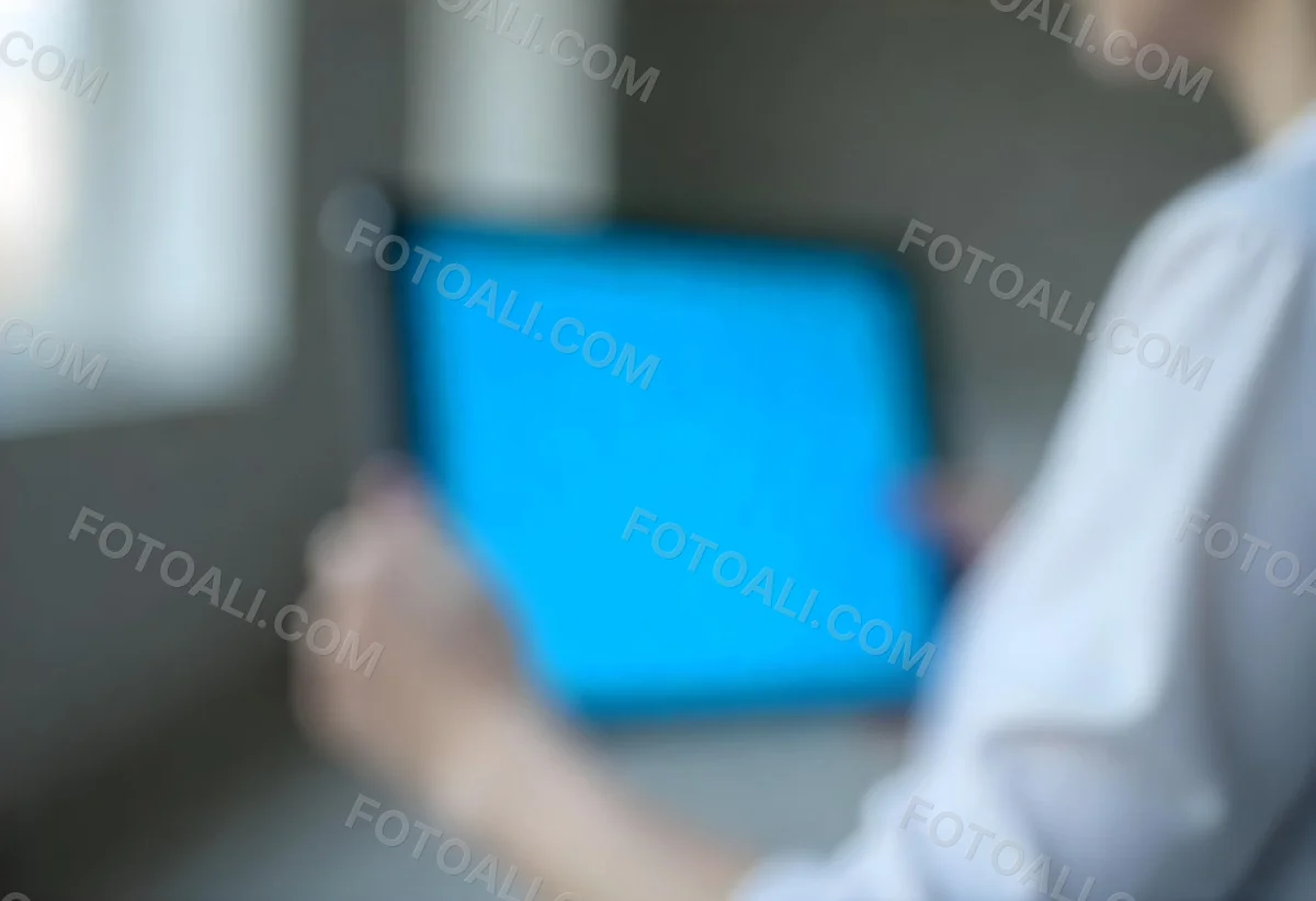 A Person Holding A Tablet With A Blank Blue Screen The Background Is Blurred And Out Of Focus The Person Is Wearing A White Shirt 2 4c89