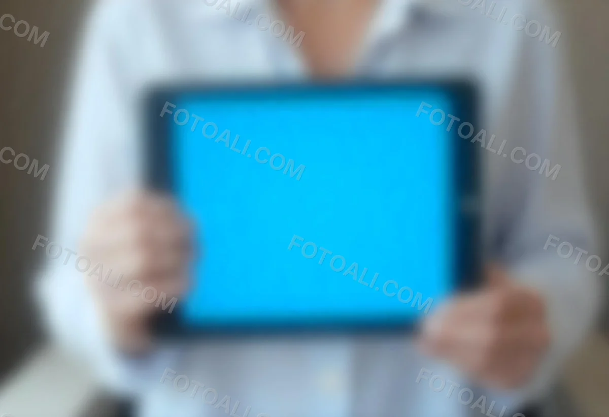 A Person Holding A Tablet With A Blank Blue Screen The Background Is Blurred And Out Of Focus The Person Is Wearing A White Shirt 4 1010