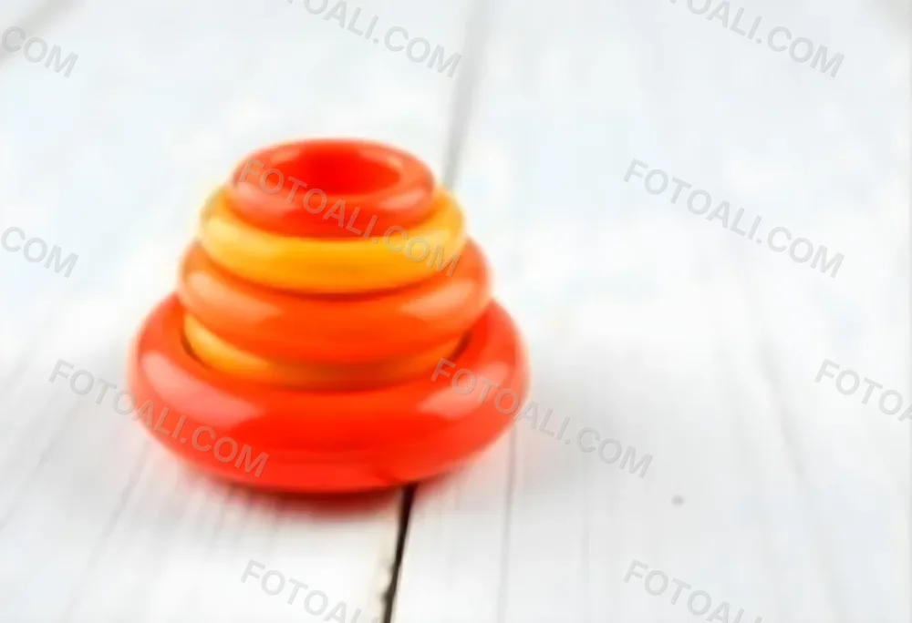 A Red Yellow And Orange Stacking Ring Toy On A White Wooden Surface The Rings Are Plastic And Shiny Close Up Shot 23 44d2