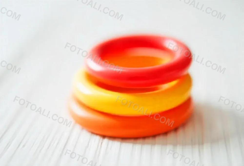 A Red Yellow And Orange Stacking Ring Toy On A White Wooden Surface The Rings Are Plastic And Shiny Close Up Shot 44 D780