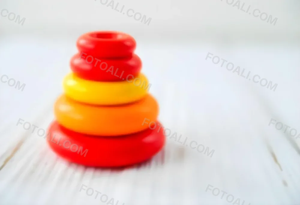 A Red Yellow And Orange Stacking Ring Toy On A White Wooden Surface The Rings Are Plastic And Shiny Close Up Shot 7 6d1d