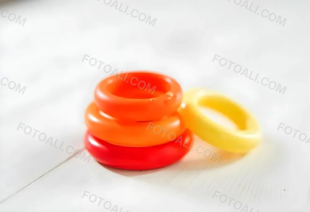 A Red Yellow And Orange Stacking Ring Toy On A White Wooden Surface The Rings Are Plastic And Shiny Close Up Shot 8 Fb10