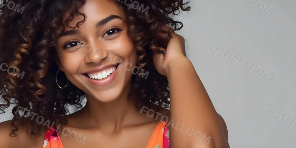 A Young Black Woman With Medium Brown Skin And Curly Hair Smiling While Touching Her Hair She Has A Bright Smile And Is Wearing A Colorful Dress The Background Is A Soft Gray 38 4922