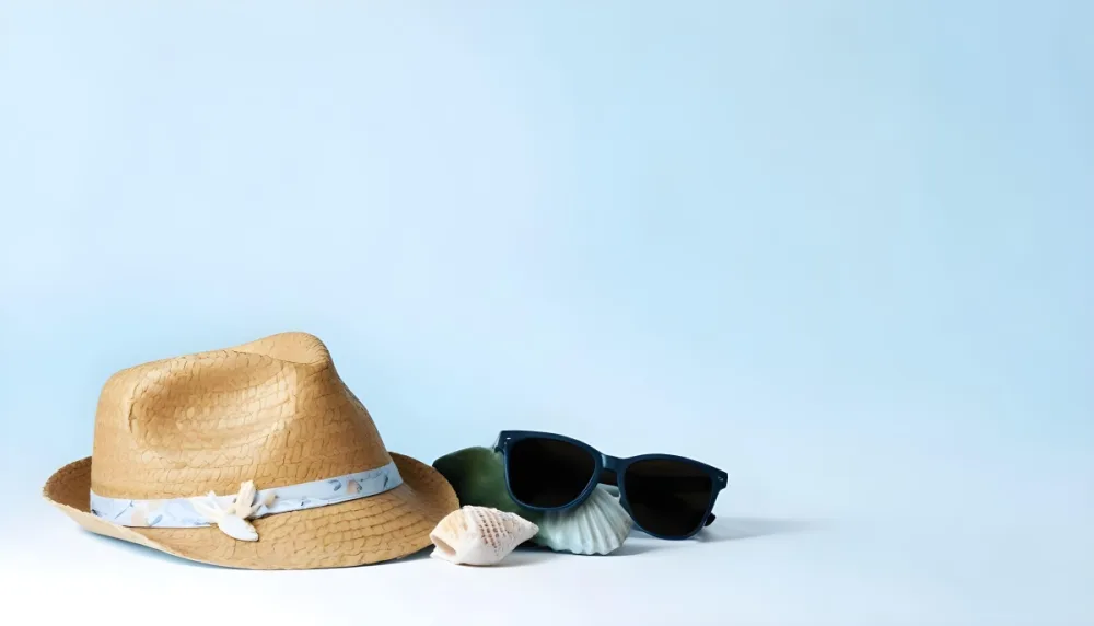 A Straw Hat With A Blue Ribbon Black Sunglasses A Seashell And A Seashell On A White Surface With A Light Blue Background 6 A21a