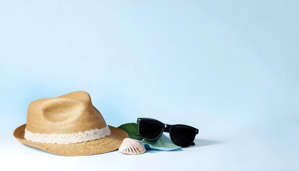 A Straw Hat With A Blue Ribbon Black Sunglasses A Seashell And A Seashell On A White Surface With A Light Blue Background 7 4c5c