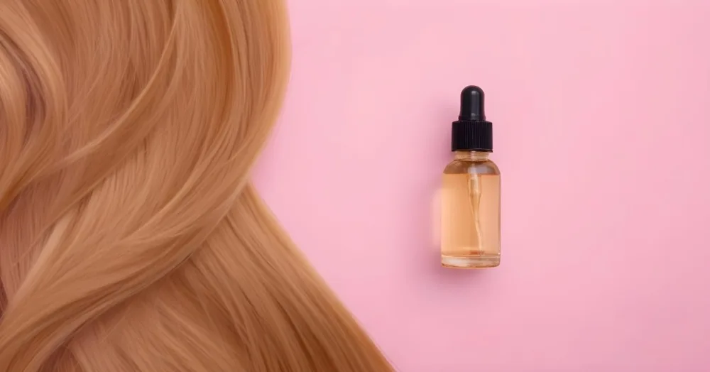 A Bottle Of Hair Oil And A Strand Of Blonde Hair On A Pink Background 2 955b