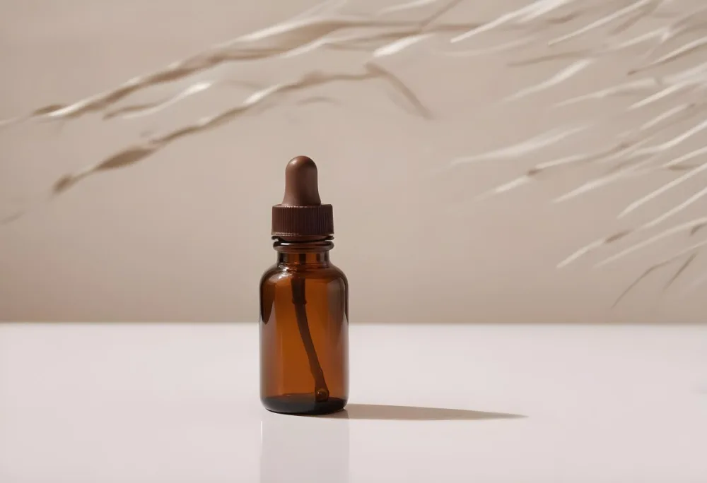 A Brown Glass Bottle With A Dropper On A White Surface With Brown Wavy Hair In The Background 3