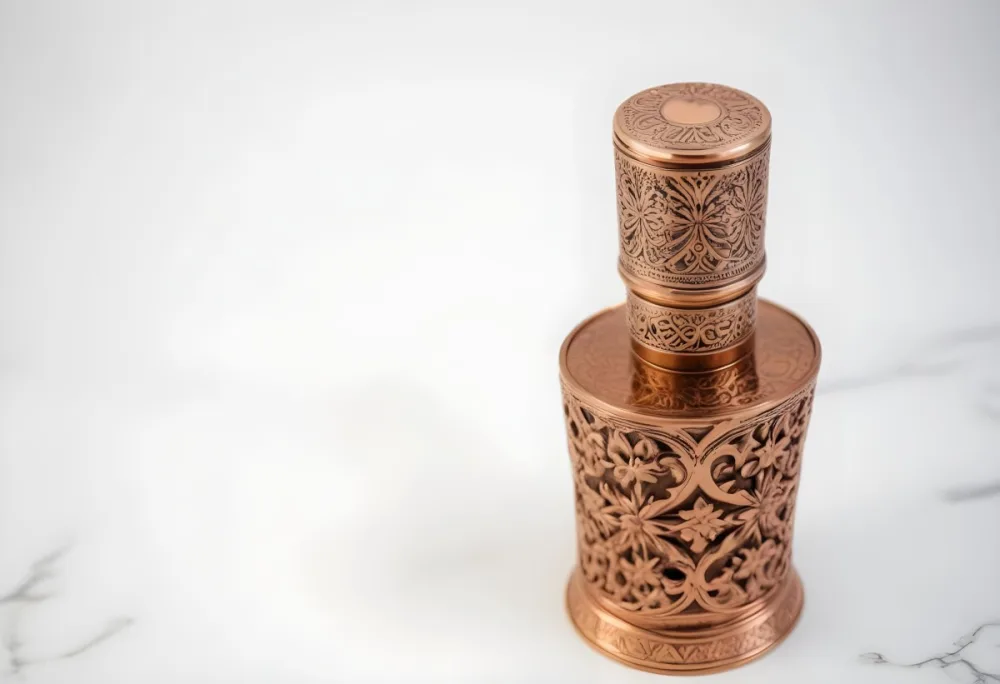 A Decorative Copper Or Bronze Perfume Bottle With An Intricate Floral And Geometric Pattern Engraved On The Surface The Bottle Has A Round Shape With A Narrow Neck And A Decorative Cap On Top Set Against A Marble Counte 26 F2dc