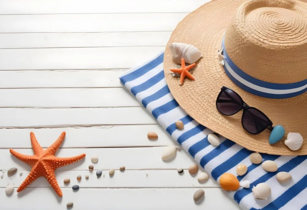A Straw Hat With A Seashell On Top Of A Striped Towel Sunglasses Sunscreen Starfish And Pebbles On A White Wooden Surface 5 4b89