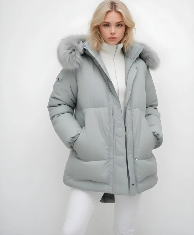 A Young Blonde Woman Wearing A Gray Puffer Jacket With A Large Fur Trimmed Hood Standing Against A White Background 25 857e