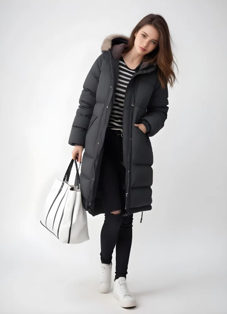 A Young Caucasian Woman With Long Brown Hair Wearing A Dark Gray Hooded Puffer Coat A Striped Shirt And Ripped Black Jeans She Is Holding A White Bag And Appears To Be Standing Outdoors In A Sunny Park 4 Ef9f