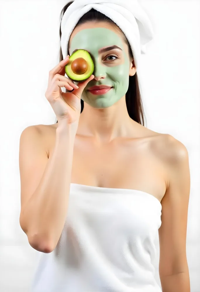 A Young Caucasian Woman With Long Dark Hair Wearing A White Towel And A Green Facial Mask Holding A Half Cut Avocado In Front Of Her Face 10 F86a