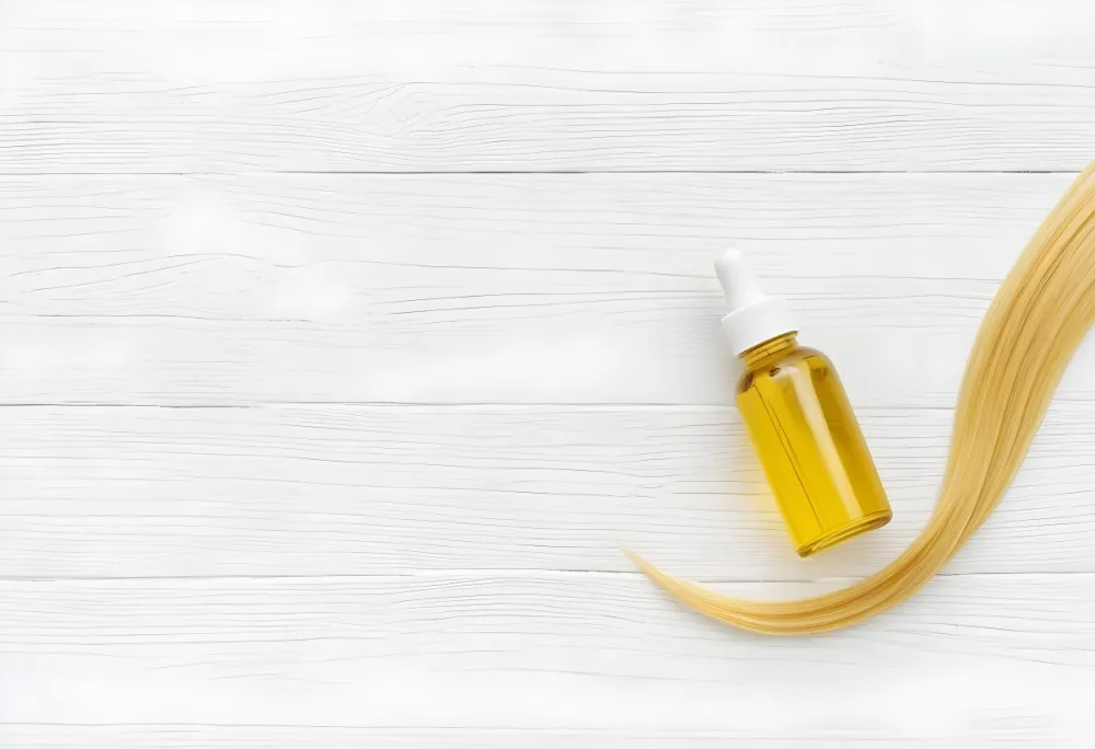 Bottle Of Yellow Hair Oil With A White Cap And A Strand Of Blonde Hair On A White Wooden Table 28 689f