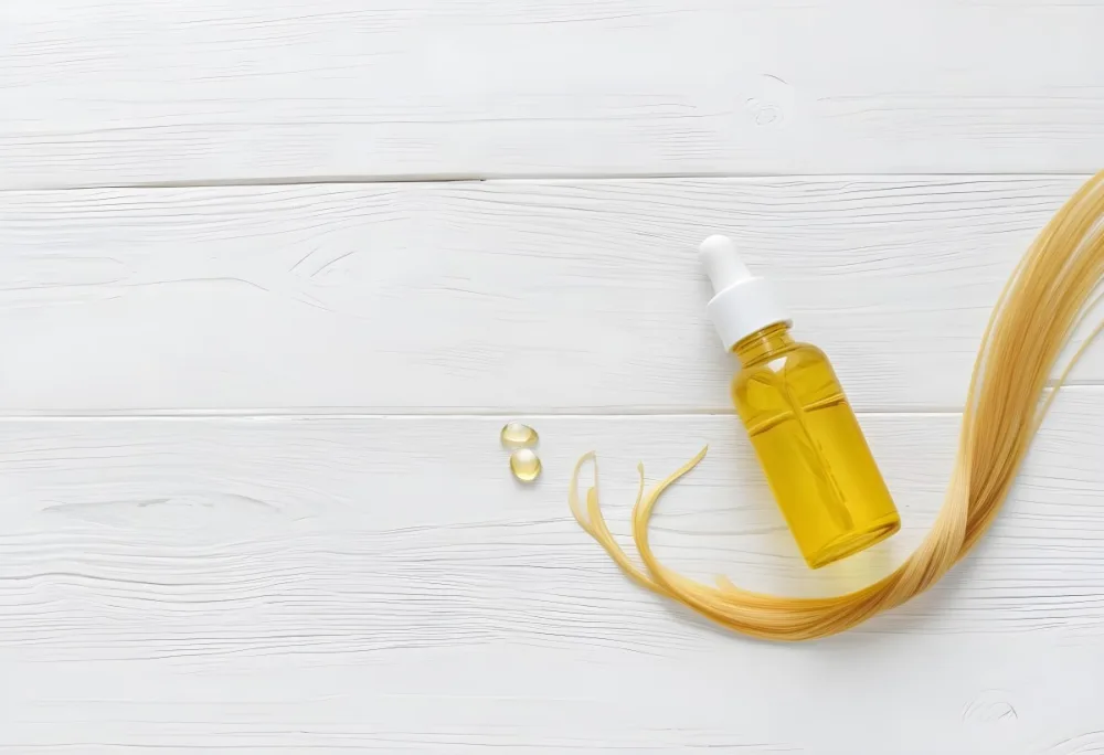 Bottle Of Yellow Hair Oil With A White Cap And A Strand Of Blonde Hair On A White Wooden Table 4 7a3f