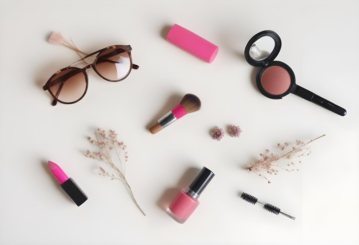 Sunglasses With Brown Lenses A Pink Hairband Pink Lipstick A Brown Lipstick Pink Nail Polish A Round Makeup Brush Small Silver Earrings Dried Flowers And False Eyelashes Arranged On A Light Colored Surface 10 5906
