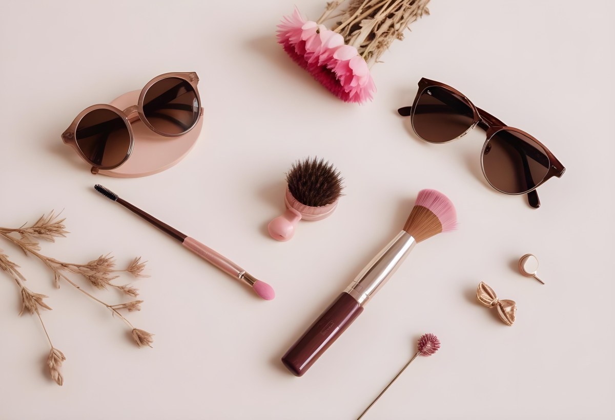 Sunglasses With Brown Lenses A Pink Hairband Pink Lipstick A Brown Lipstick Pink Nail Polish A Round Makeup Brush Small Silver Earrings Dried Flowers And False Eyelashes Arranged On A Light Colored Surface 3 6fac