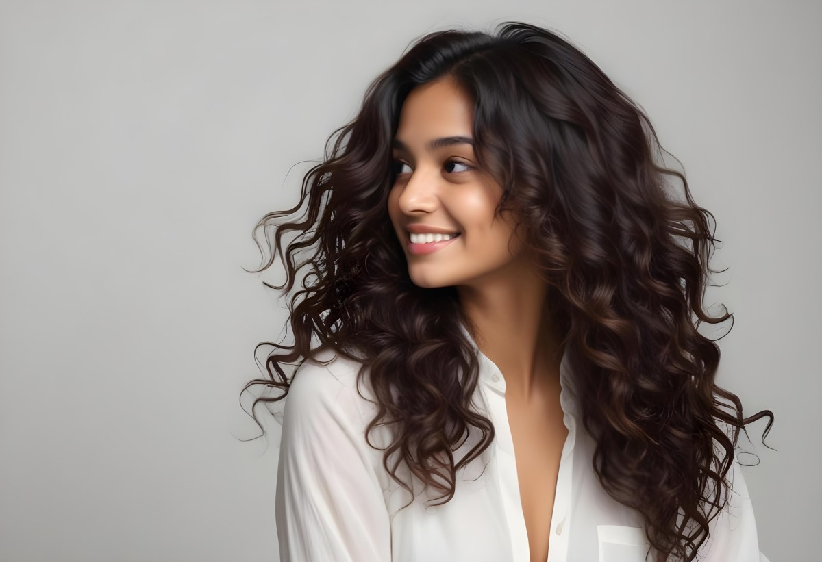 Young Woman Of South Asian Descent With Long Curly Dark Brown Hair Smiling Softly She Is Wearing A White Blouse And Has A Light Background 28 703c