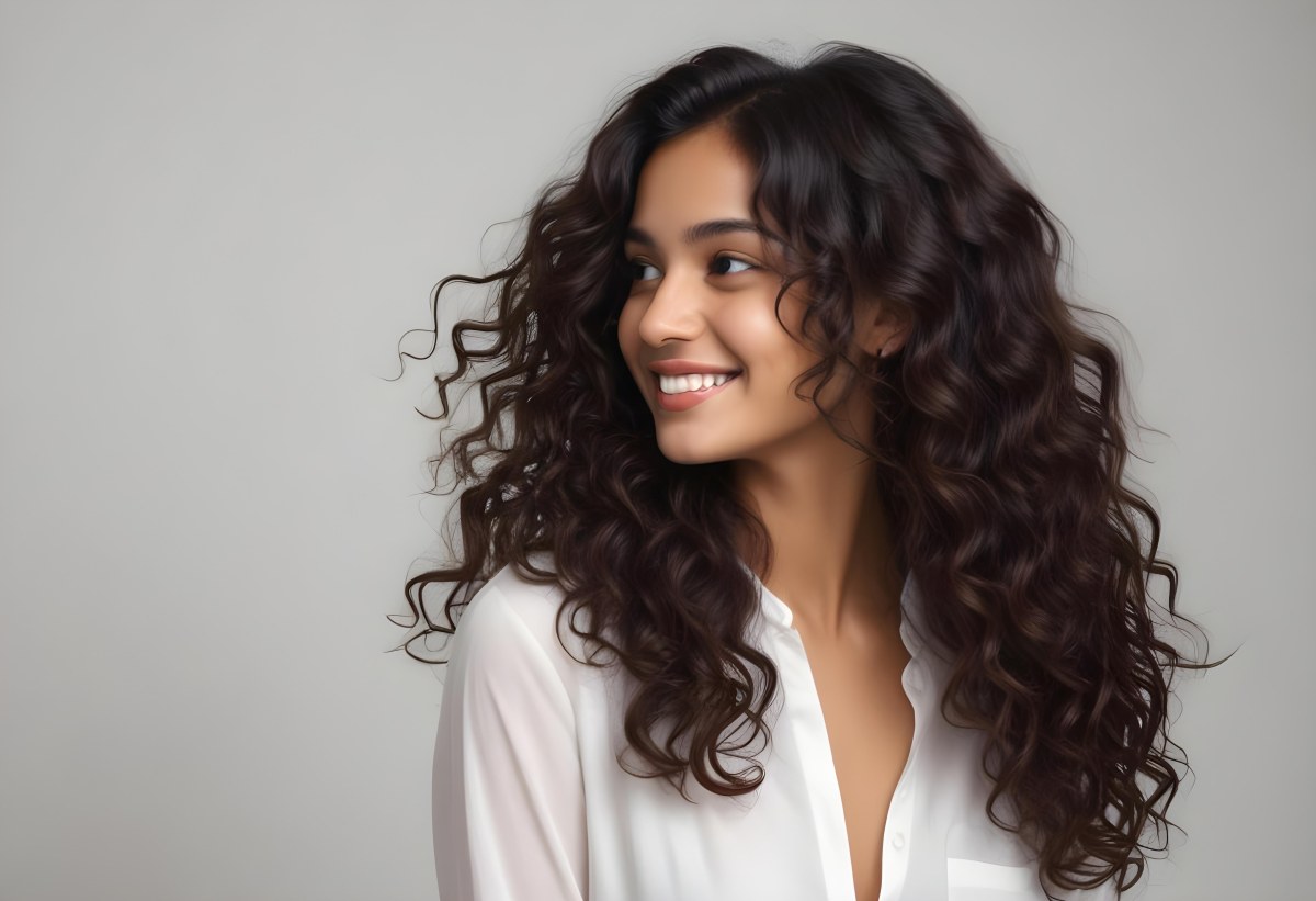 Young Woman Of South Asian Descent With Long Curly Dark Brown Hair Smiling Softly She Is Wearing A White Blouse And Has A Light Background 62 D667