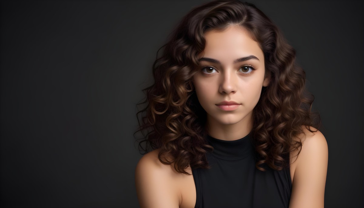 Young Woman With Medium Skin Tone And Long Curly Brown Hair Wearing A Black Sleeveless Top Looking Directly At The Camera With A Neutral Expression The Background Is Dark And Simple Emphasizing Her Features 63 57ec