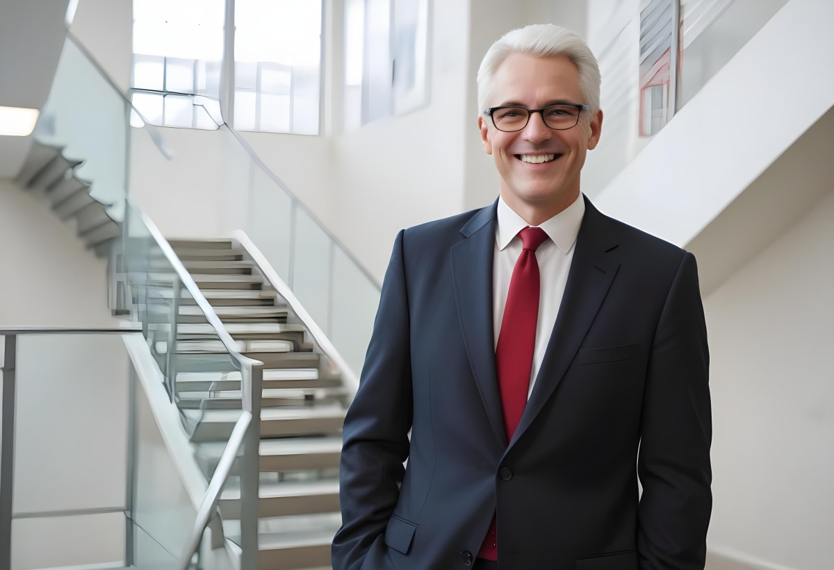 White Man 50 Years Old With White Hair And Glasses Wearing A Suit And A Red Tie Smiling In An Office Environment With A Staircase In The Background 11 6b32