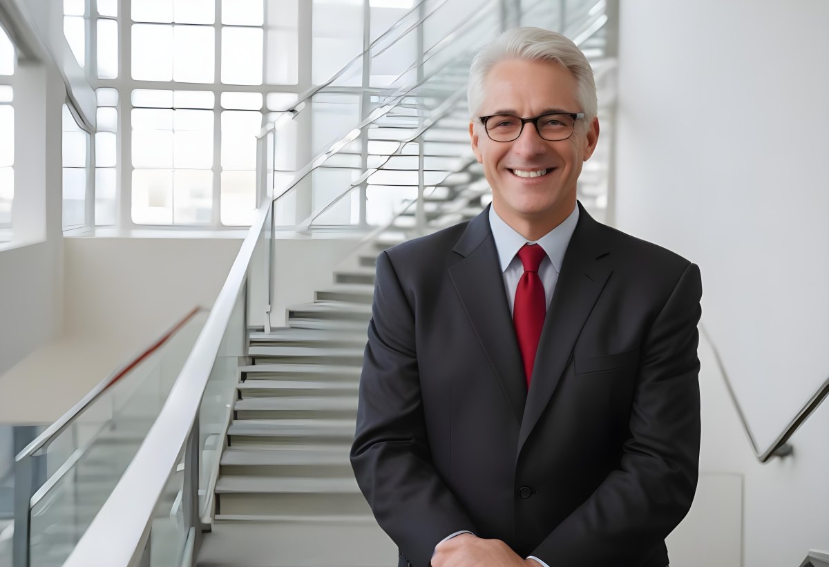 White Man 50 Years Old With White Hair And Glasses Wearing A Suit And A Red Tie Smiling In An Office Environment With A Staircase In The Background 9 E30f