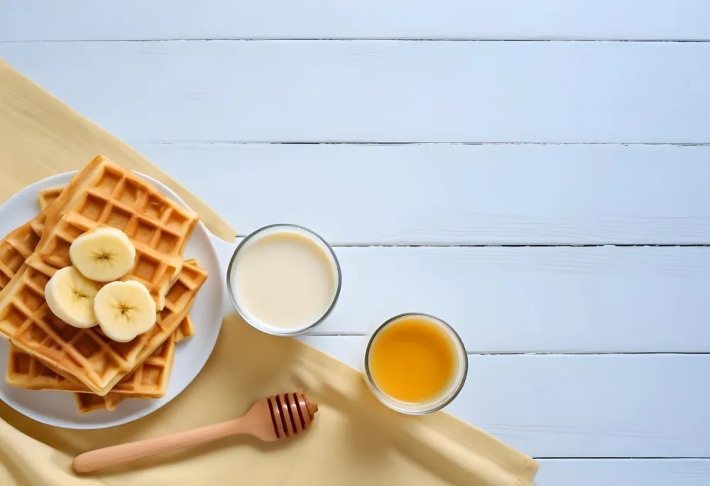 Waffles With Banana Slices On A Glass Plate A Glass Of Milk A Bowl Of Honey And A Wooden Dipper On A White Cloth Over A White Wooden Table 13 7515