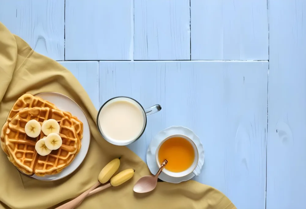 Waffles With Banana Slices On A Glass Plate A Glass Of Milk A Bowl Of Honey And A Wooden Dipper On A White Cloth Over A White Wooden Table 20 079c