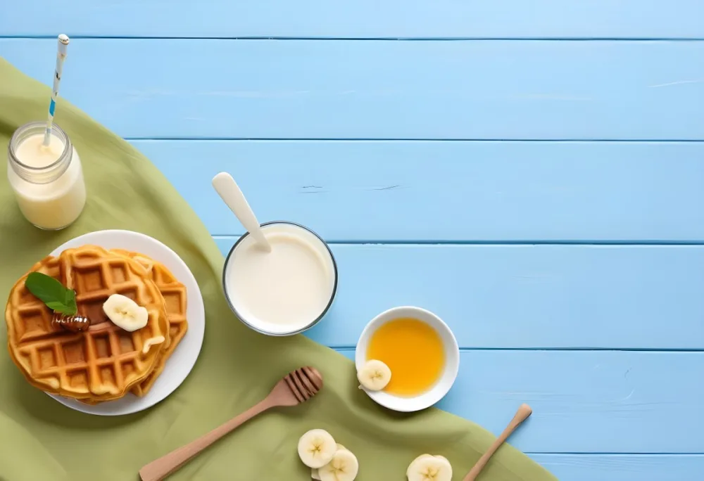 Waffles With Banana Slices On A Glass Plate A Glass Of Milk A Bowl Of Honey And A Wooden Dipper On A White Cloth Over A White Wooden Table 34 D89b