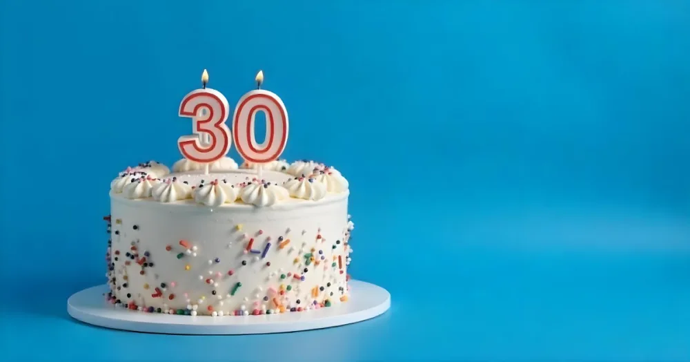 A 30th Birthday Cake With Candles On Top White Frosting And Sprinkles On A Blue Background 1 F733