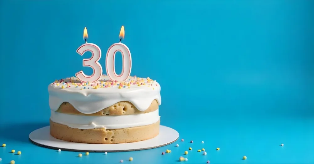 A 30th Birthday Cake With Candles On Top White Frosting And Sprinkles On A Blue Background 11 4f15