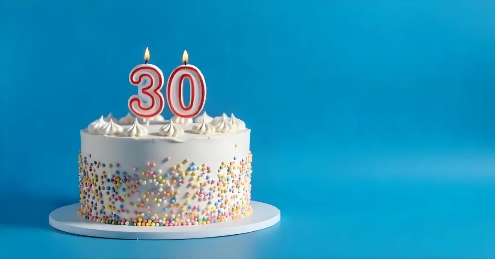 A 30th Birthday Cake With Candles On Top White Frosting And Sprinkles On A Blue Background 15 8033