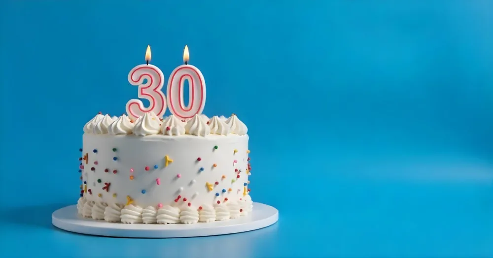 A 30th Birthday Cake With Candles On Top White Frosting And Sprinkles On A Blue Background 9 9e4c