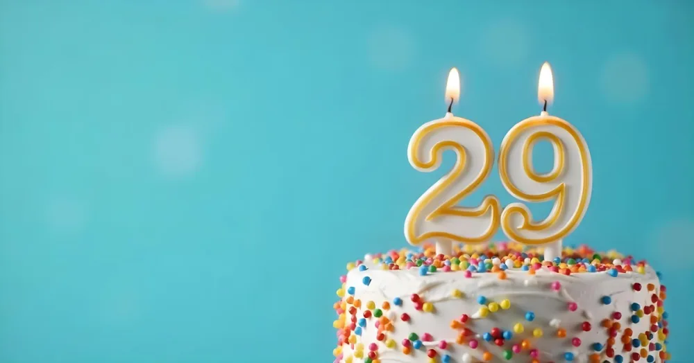 A Cake With White Frosting And Colorful Sprinkles Topped With A Candle In The Shape Of The Number 29 Blue Background 1 3353