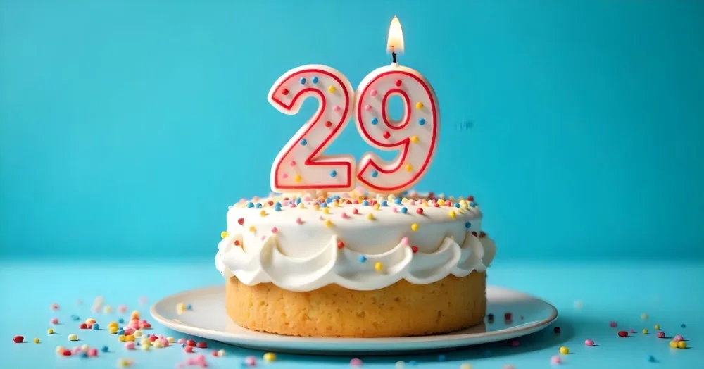 A Cake With White Frosting And Colorful Sprinkles Topped With A Candle In The Shape Of The Number 29 Blue Background 12 77fb