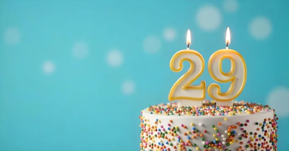 A Cake With White Frosting And Colorful Sprinkles Topped With A Candle In The Shape Of The Number 29 Blue Background 13 7234