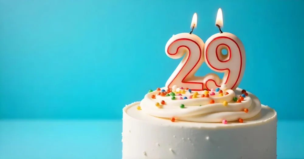 A Cake With White Frosting And Colorful Sprinkles Topped With A Candle In The Shape Of The Number 29 Blue Background 18 4012