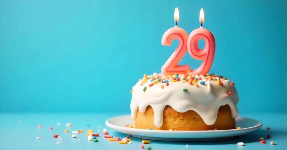 A Cake With White Frosting And Colorful Sprinkles Topped With A Candle In The Shape Of The Number 29 Blue Background 21 Fde6