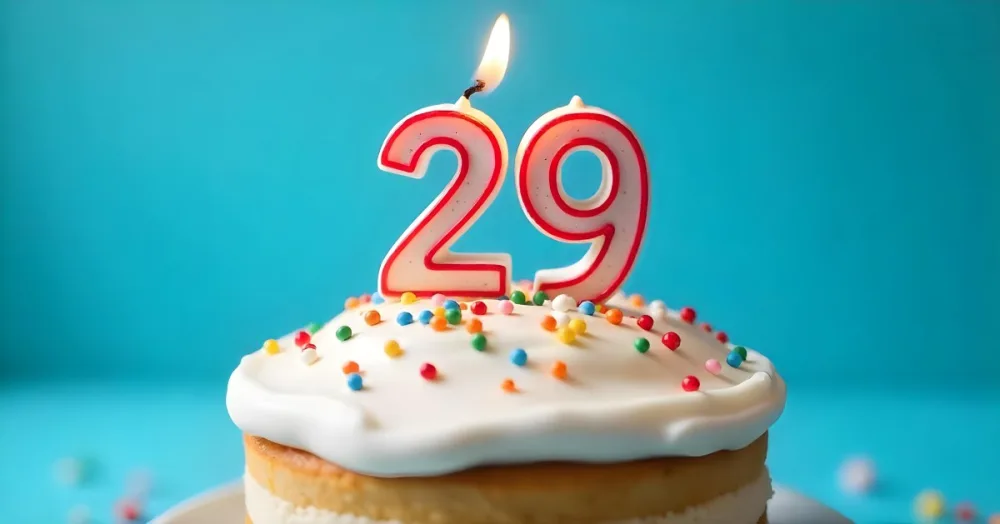 A Cake With White Frosting And Colorful Sprinkles Topped With A Candle In The Shape Of The Number 29 Blue Background 23 D56b