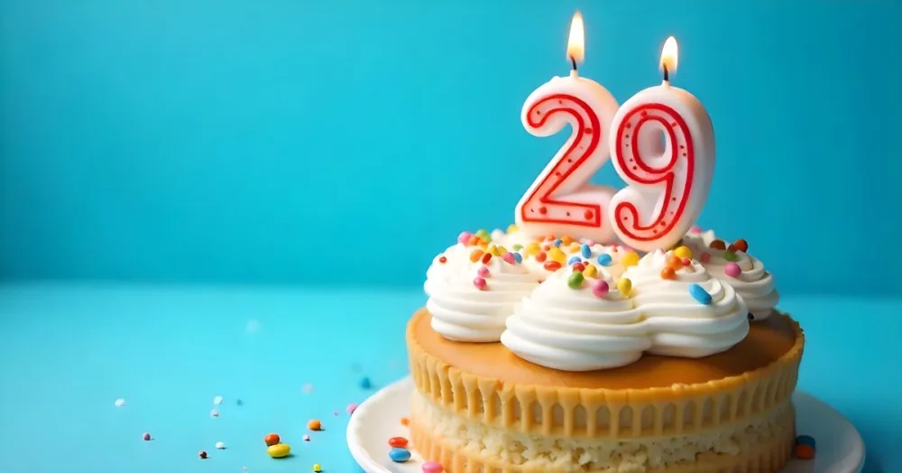 A Cake With White Frosting And Colorful Sprinkles Topped With A Candle In The Shape Of The Number 29 Blue Background 24 A7c6