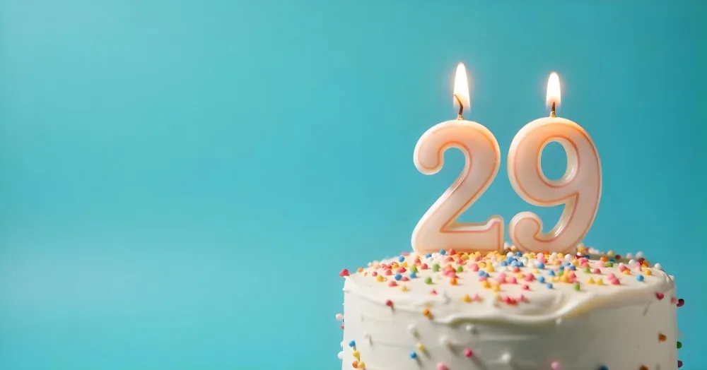 A Cake With White Frosting And Colorful Sprinkles Topped With A Candle In The Shape Of The Number 29 Blue Background 27 02aa