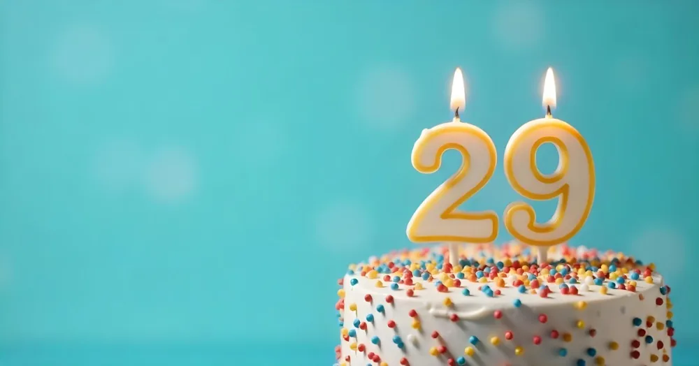 A Cake With White Frosting And Colorful Sprinkles Topped With A Candle In The Shape Of The Number 29 Blue Background 3 43d5