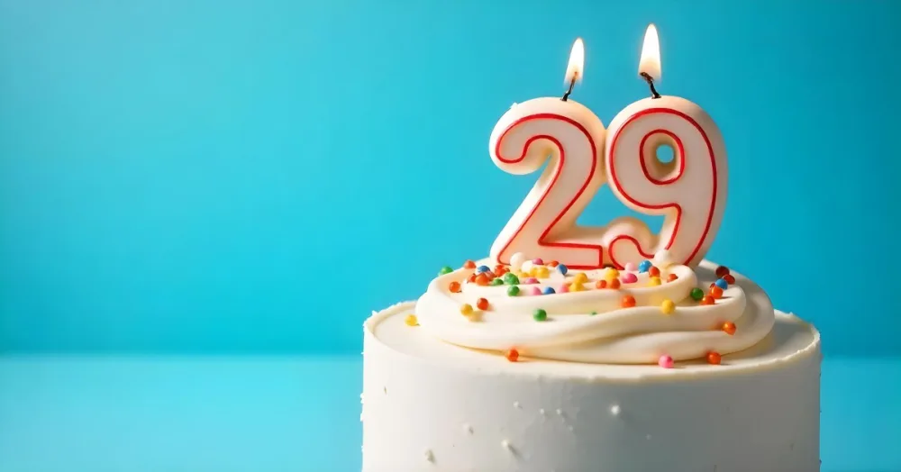 A Cake With White Frosting And Colorful Sprinkles Topped With A Candle In The Shape Of The Number 29 Blue Background 30 554f