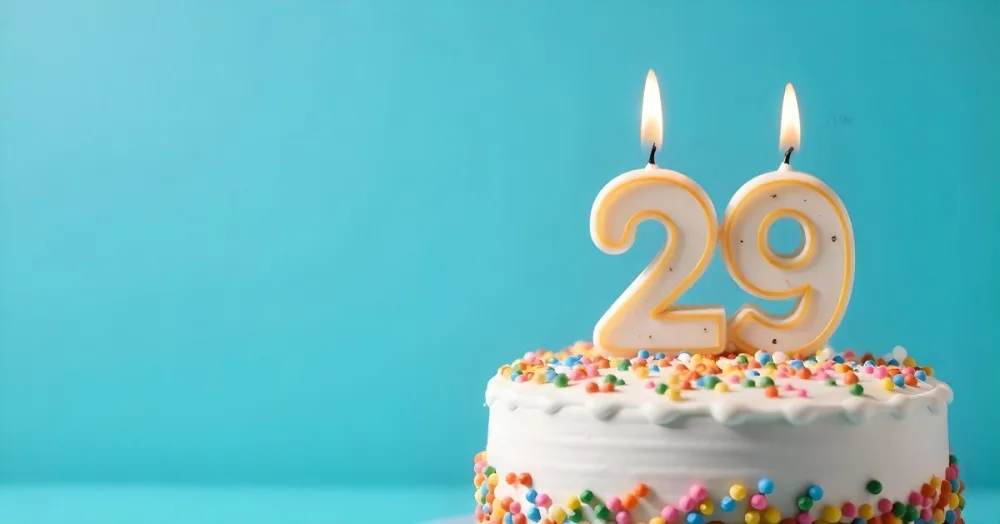 A Cake With White Frosting And Colorful Sprinkles Topped With A Candle In The Shape Of The Number 29 Blue Background 32 0d28