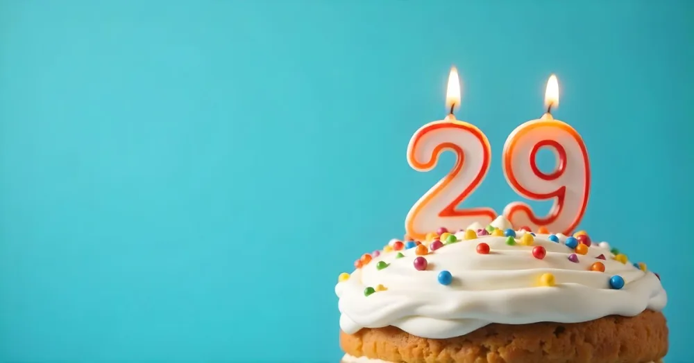 A Cake With White Frosting And Colorful Sprinkles Topped With A Candle In The Shape Of The Number 29 Blue Background 33 D551