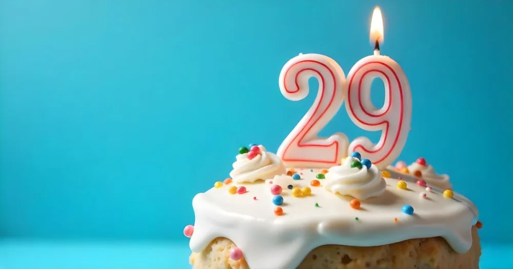 A Cake With White Frosting And Colorful Sprinkles Topped With A Candle In The Shape Of The Number 29 Blue Background 34 F684