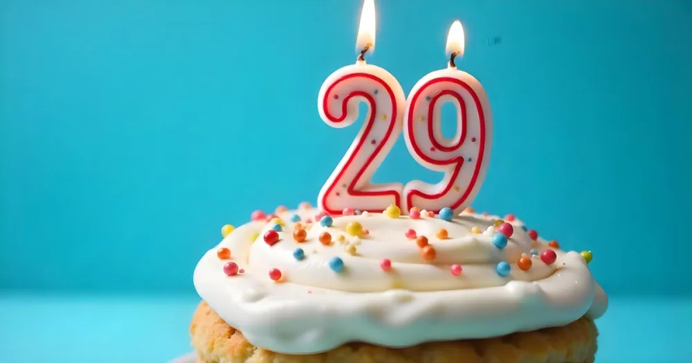 A Cake With White Frosting And Colorful Sprinkles Topped With A Candle In The Shape Of The Number 29 Blue Background 6 0893