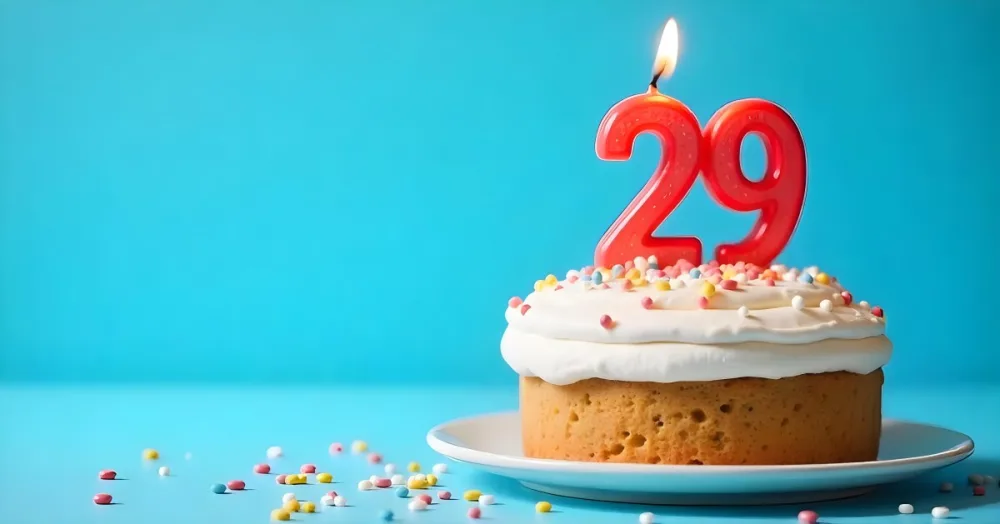 A Cake With White Frosting And Colorful Sprinkles Topped With A Candle In The Shape Of The Number 29 Blue Background 8 8c76