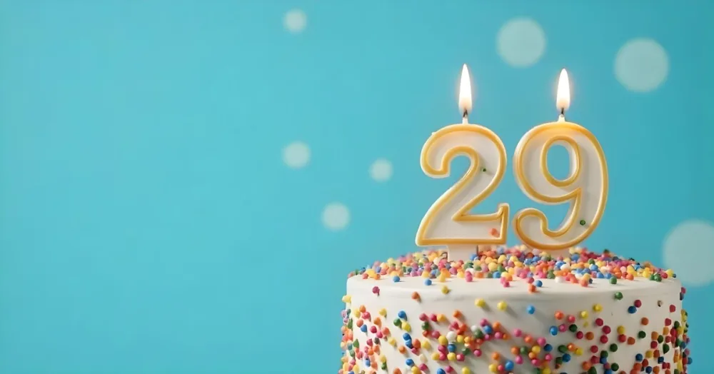 A Cake With White Frosting And Colorful Sprinkles Topped With A Candle In The Shape Of The Number 29 Blue Background 9 7cd2