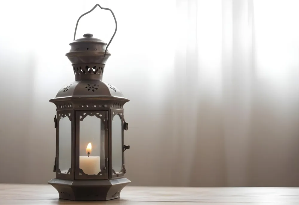 An Antique Metal Lantern With Glass Panels Sits On A Glass Surface A Candle Burning Inside Against A Blurred White Background 13 2a4f